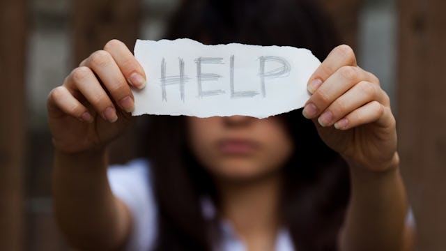 A teenage girl holding a paper reading, "HELP"