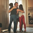 A father hugging his son and daughter in a living room 