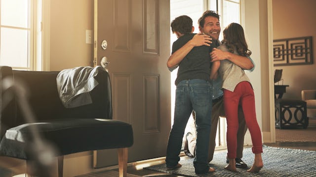 A father hugging his son and daughter in a living room