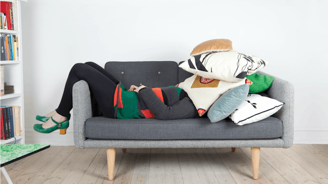 A woman lying down on a sofa fully covered with pillows during National Moms' Day off