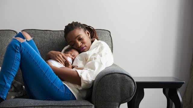 A woman wearing a white shirt and jeans hugging and sleeping with her two month old newborn on a gra...
