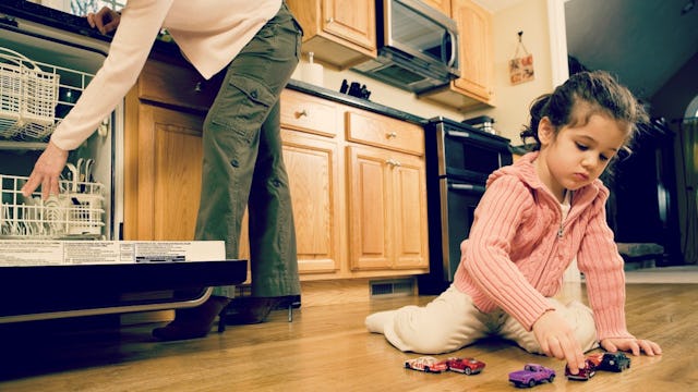 A mom putting dishes in a dishwasher while her kid is playing behind her