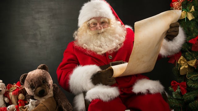 Santa Claus in his traditional suit, holding his letter to kids with autism with toys beside him