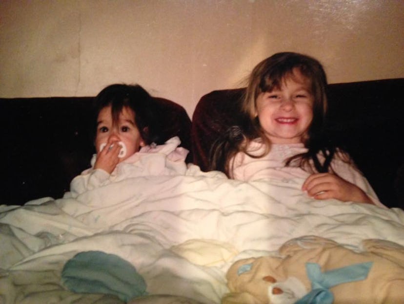 Sarah Hosseini and her sister as children lying in a bed