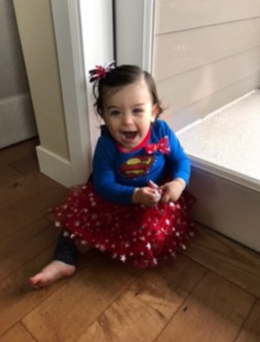 A little girl smiling and wearing a superman shirt with a red skirt