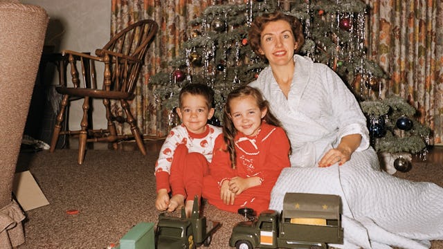 A single mother in a white dress sitting with her son and daughter in front of a Christmas tree with...