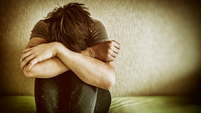 A teen struggling with depression sitting on the floor with head on his knees