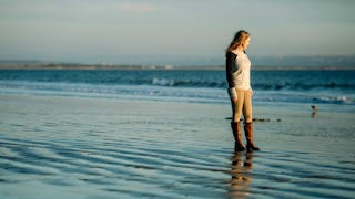 A divorced woman wearing a white shirt, yellow pants and brown boots standing at the shallow part of...