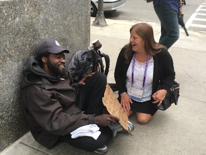 A woman sitting with a homeless man on the street