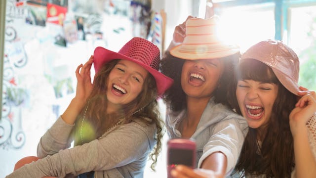 Three girls taking a selfie, two wearing cowboy hats, and one is wearing a cap while they are mockin...