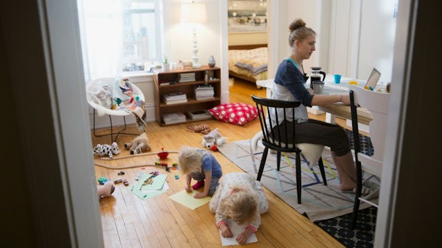 Mother working on laptop while her two toddlers are drawing pictures on the floor in a living room