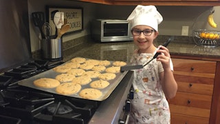 chopped junior, little girl stands beside oven tray of cookies