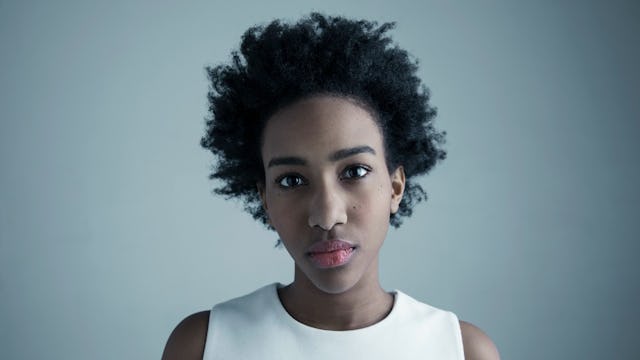 A portrait of a woman with a curly black afro in a white tank top