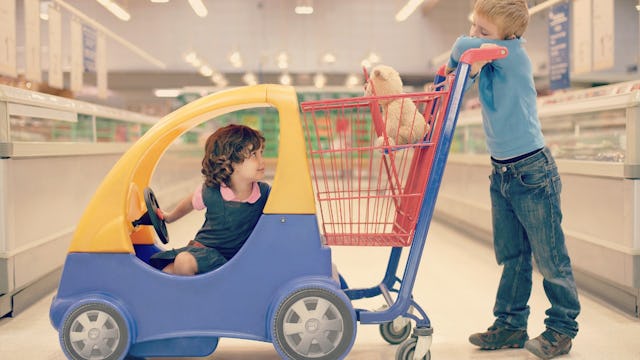 Little girl sitting in a grocery store car cart while boy drives her around