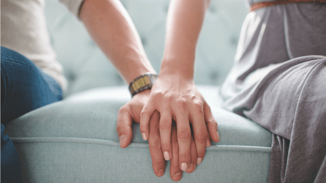 A man and a woman sitting on a sofa, her hand is over the man's hand