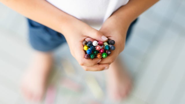 A boy holding multiple wax crayons of various colors in his hands.