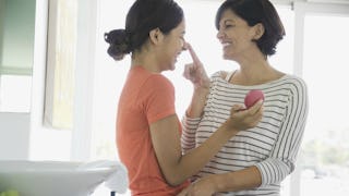 A mother in a white sweater and black stripes touching the nose of her daughter in an orange T-shirt...