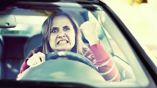 A mature blonde woman in a red shirt is raging while standing in a car line