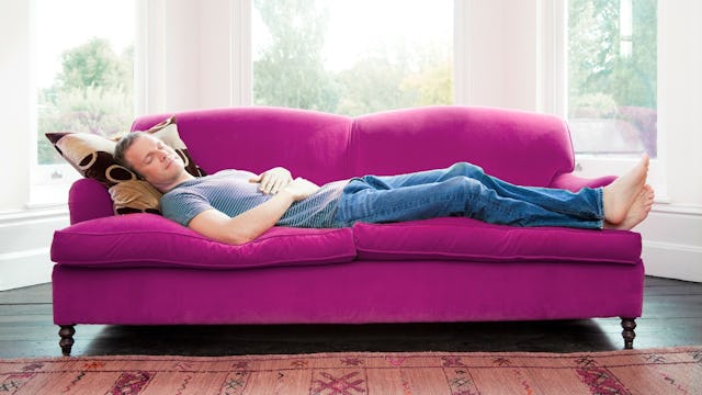 A husband is napping on an orchid couch 