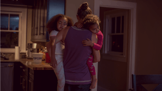 An exhausted mom carrying her two sleeping daughters, showing the invisible workload of motherhood