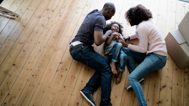 A family of a mom, dad, and daughter tickling each other on the floor of a family home