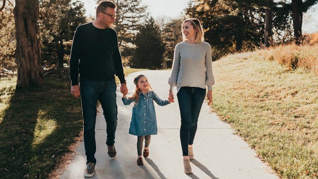 A couple strolling through the park while holding their daughter's hand