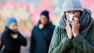 A woman with a cold blowing her nose in public and trying to stay away from kids because she's sick