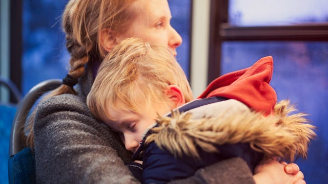 A parent in a grey jacket holding and hugging her kid with special needs in a bus