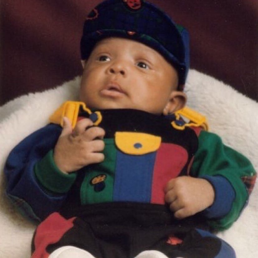 Trease Shine Hinton's son as a baby wearing multi-colored overalls and a cap