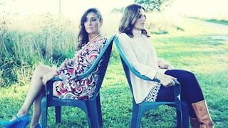 Two moms sitting back to back on chairs in a park during a sunny day, because they do not want to of...