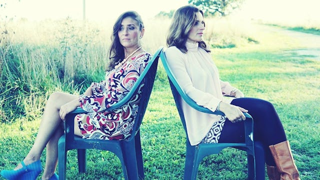 Two moms sitting back to back on chairs in a park during a sunny day, because they do not want to of...