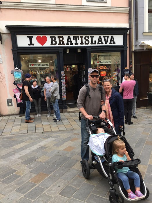 Mother and father pushing two kids in a baby stroller with one kid sleeping and a sign above with te...