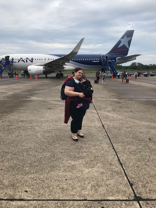 Mother wearing a black shirt standing in front of a blue and white plane while carrying her child