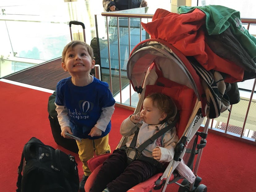 One very excited sibling while the other sleeps in the stroller, both surrounded by luggage 