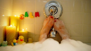 A woman taking a bubble bath with cannabis-infused products with candles placed in one corner of the...