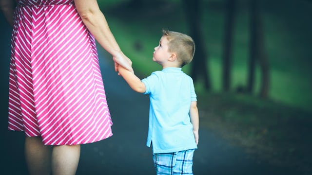 A mom in a pink-white striped dress and her son in a blue shirt and shorts standing and holding hand...