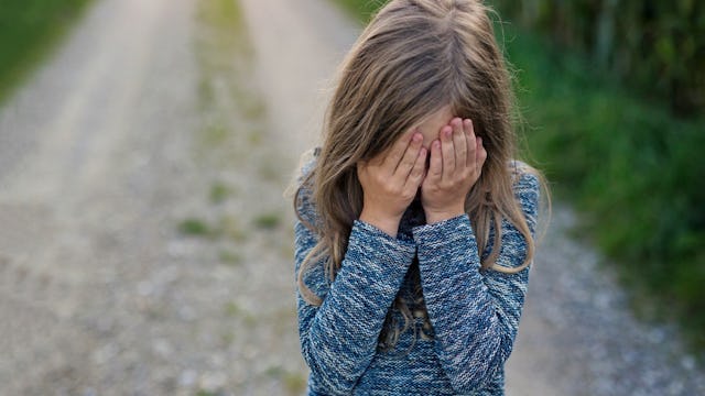 A little girl covering her face with hands while crying after experiencing a childhood emotional abu...
