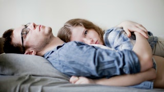 A brunette woman in a blue checked shirt lying on top of her husband wearing a blue denim shirt wear...