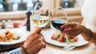 Two people toasting with glasses of black and white wine while eating a meal in a restaurant