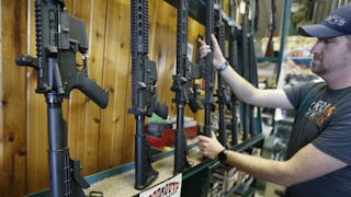 A man wearing a gray cap and a gray T-shirt and a watch picking up a riffle in a gun shop