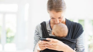 A mother using facebook on her phone while holding and kissing her son in a hug and cuddle adjustabl...