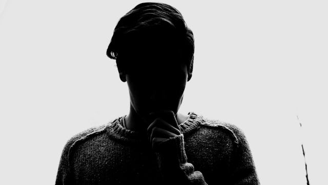 A person holding their pointer finger over their mouth in a dark room with a white background