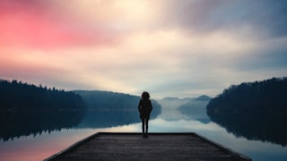 A woman standing on a pier with a lake in front of her 