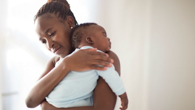 A mother holding and hugging her baby with its head on her shoulder