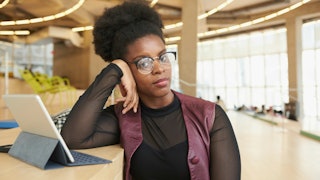 A black-haired curly liberal woman with glasses in a black tulle shirt and burgundy leather waistcoa...
