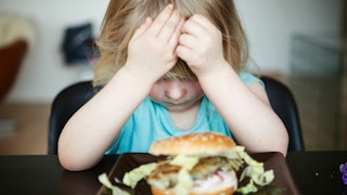 A picky eater kid sitting at the dining table and refusing to eat the sandwich placed in front of he...