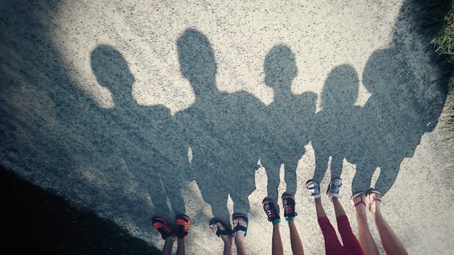 Five pairs of feet standing on the road, and their large shadows visible on the road