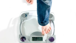 A young child stepping on a digital glass scale while wearing blue jeans