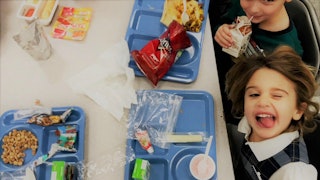 Two kids eating food in the school cafeteria and smiling