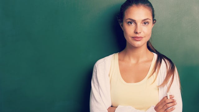 A brunette woman with her hair tied up in a ponytail, wearing a white shirt and a yellow top